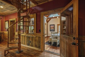 A wooden interior with a spiral staircase, wooden walls, and a door leading to a room with a chair and a painting. - Dual Blue Ridge Cabins, sleeps 14, large yard, dogs welcome! (Blue Ridge)