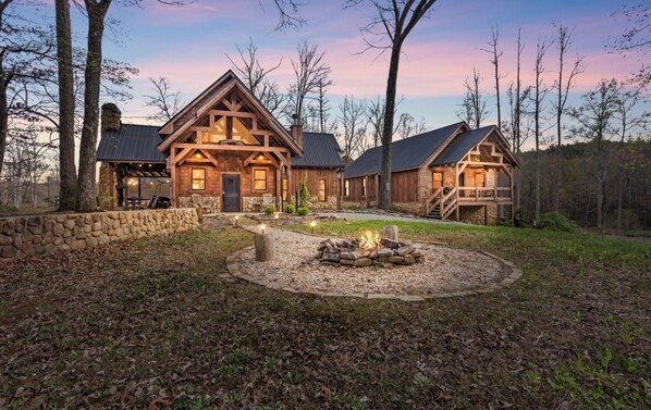 A rustic cabin with a stone wall, a fire pit, and a covered outdoor seating area. - Dual Blue Ridge Cabins, sleeps 14, large yard, dogs welcome! (Blue Ridge)