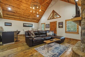 A cozy living room with a leather sofa, a coffee table, and a fireplace. There are framed pictures on the walls and a wooden ceiling. - Dual Blue Ridge Cabins, sleeps 14, large yard, dogs welcome! (Blue Ridge)