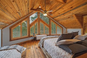 A high-ceilinged attic bedroom with a sloped roof, large windows, and a ceiling fan. - Dual Blue Ridge Cabins, sleeps 14, large yard, dogs welcome! (Blue Ridge)