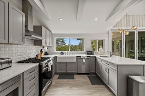 Una cocina moderna con armarios grises, estufa de acero inoxidable y ventana con vista a árboles.