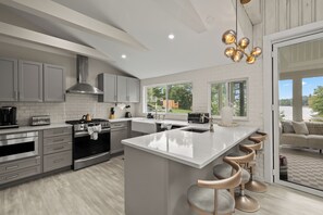 A modern kitchen with a central island, stainless steel appliances, and a view to the outdoors. - Lakeshore Retreat-Modern Lakefront Home w/ Hot Tub (Monticello)