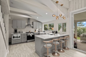 Una cocina moderna con una isla central, taburetes de bar y vistas al exterior.