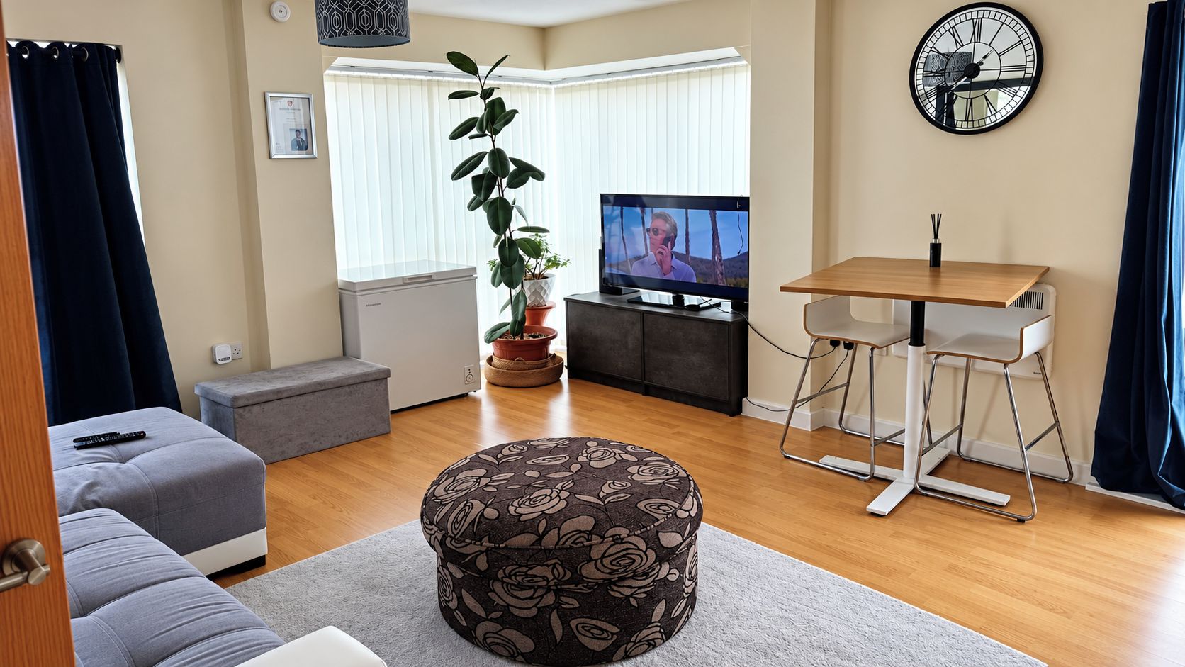 Un salon comprenant un canapé, un pouf, un téléviseur, une table à manger et des plantes en pot.
