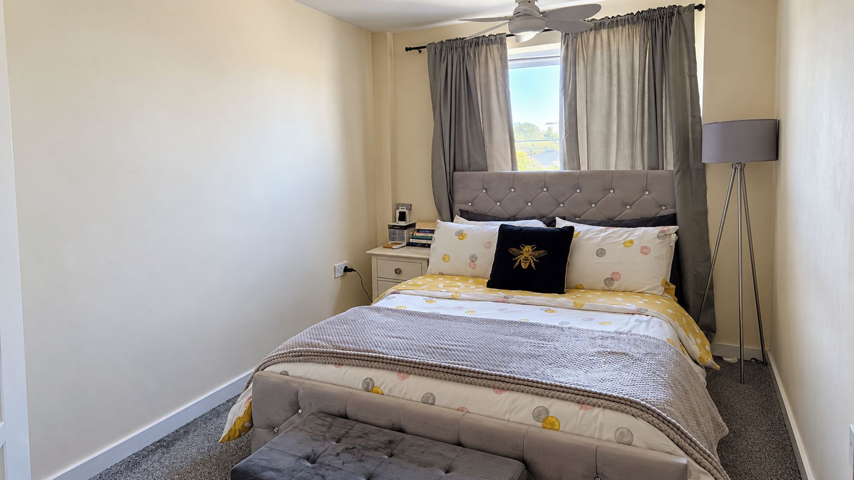 Une chambre à coucher avec un lit, une table de chevet, une lampe et une fenêtre avec des rideaux.