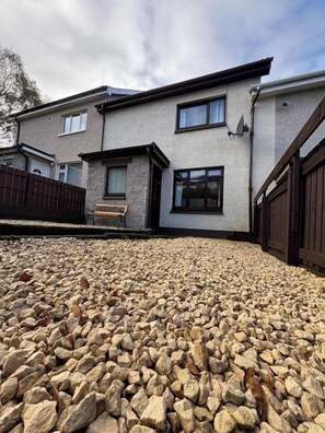 A two-story house with a stone facade, a wooden deck, and a metal gate. - House Sleeps 4 with Enclosed Garden (Oban)