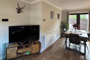 A living room with a flat-screen TV, wooden cabinet, dining table with chairs, and a mounted deer head. - House Sleeps 4 with Enclosed Garden (Oban)