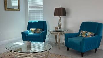 A living room with two blue armchairs, a glass coffee table, a lamp, and a mirror on the wall.