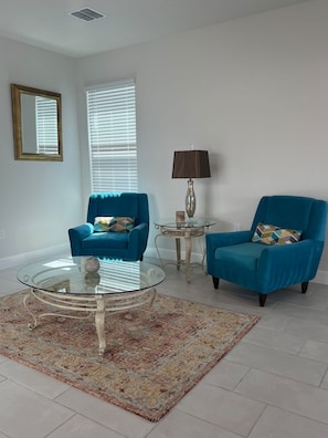 A living room with two blue armchairs, a glass coffee table, a lamp, and a mirror on the wall. - LUX Mins to HCA, Advent & Gemini Springs Beautiful 4 bedroom brand new home (DeBary)