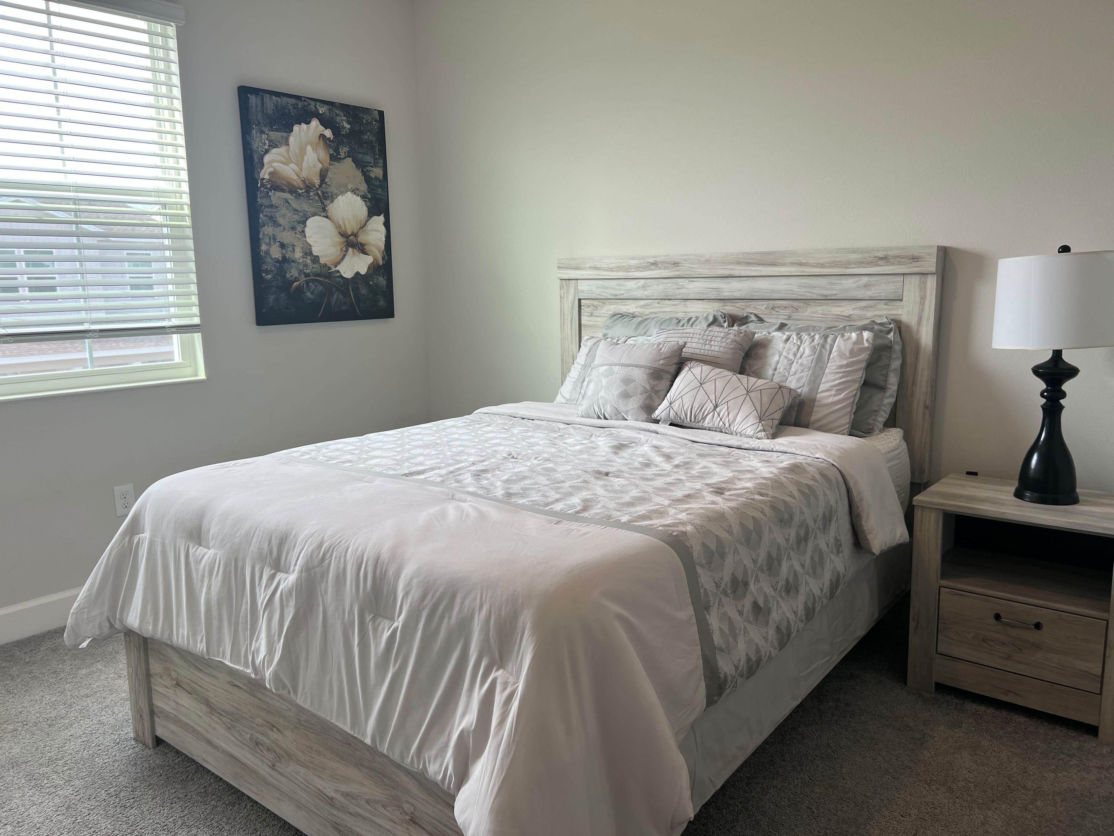 A bedroom with a bed, nightstand, lamp, and artwork.