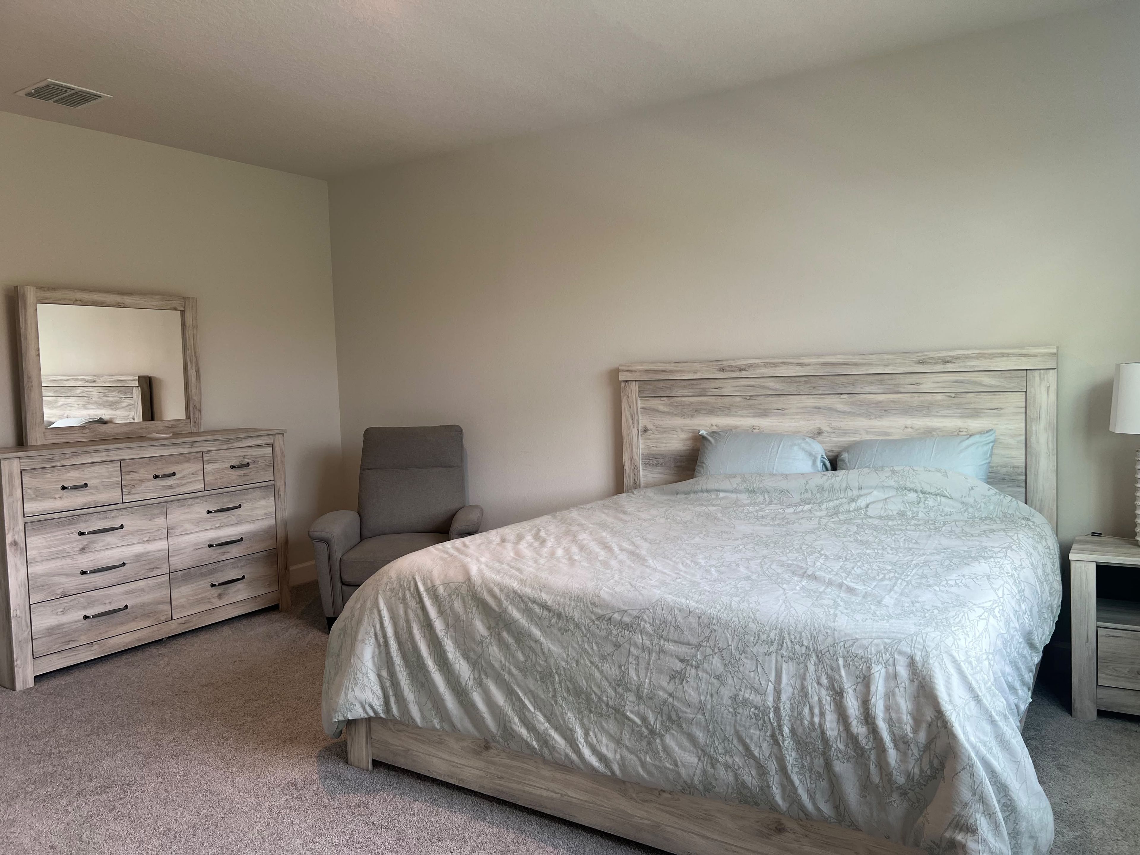 A bedroom with a bed, a dresser, a chair, and a nightstand.
