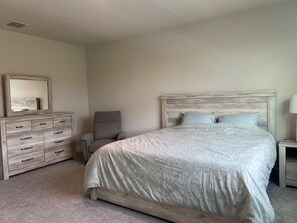 Un dormitorio con cama, cómoda, silla y mesita de noche.