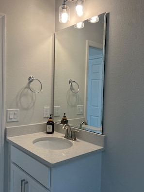 A bathroom with a large mirror, a sink, and a door visible in the reflection. - LUX Mins to HCA, Advent & Gemini Springs Beautiful 4 bedroom brand new home (DeBary)