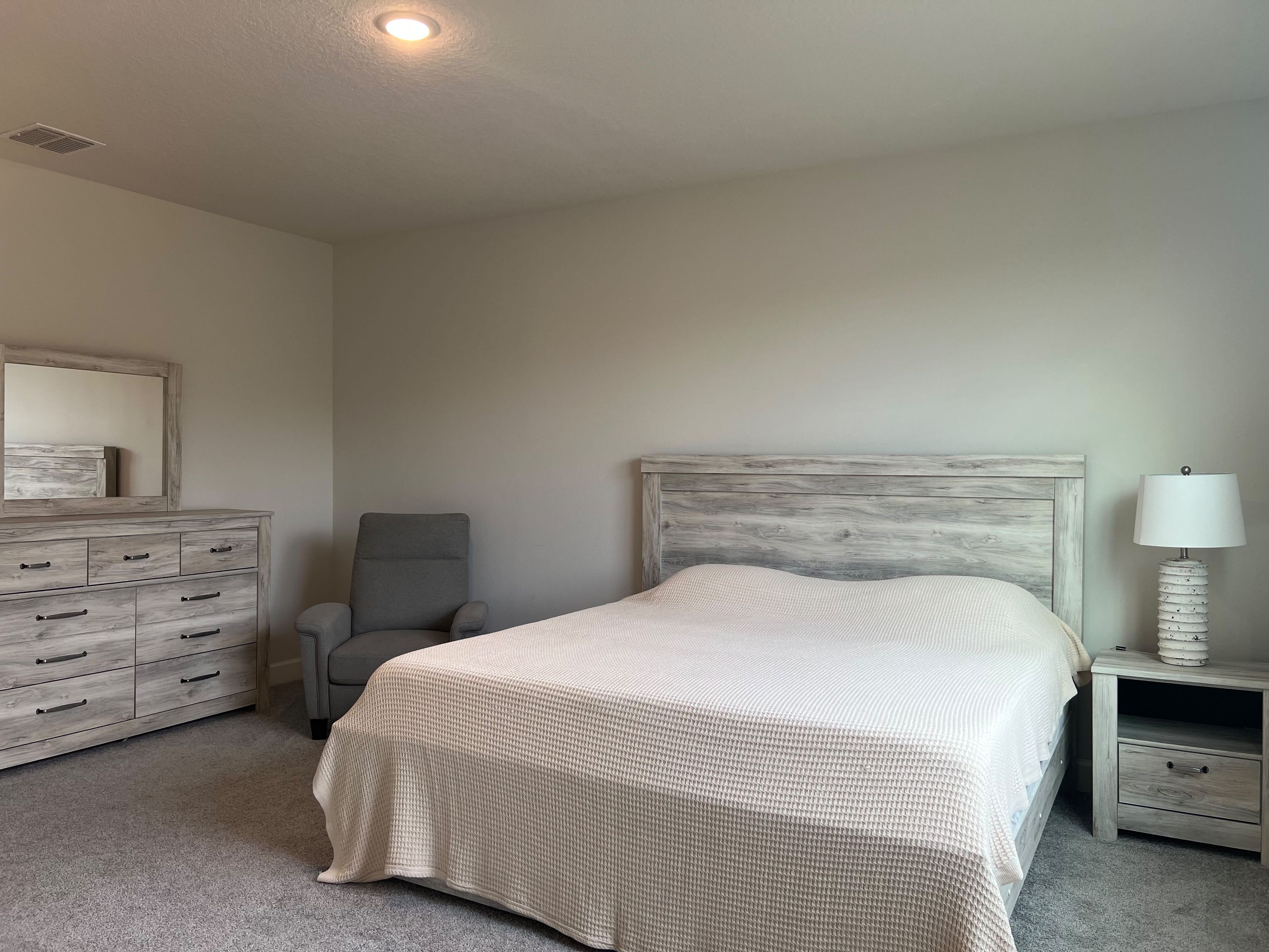 A bedroom with a bed, a dresser, a chair, and a nightstand.