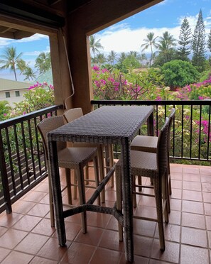 Ein Balkon mit Tisch und Stühlen, der auf einen Garten mit verschiedenen Pflanzen und Blick auf das Meer hinausblickt.