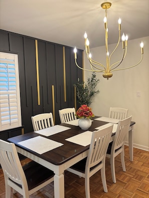 A dining area with a dark wooden table, white chairs, a chandelier, and a vase with flowers. - Private bathroom + bedroom UNC & Duke Hospital (Durham)