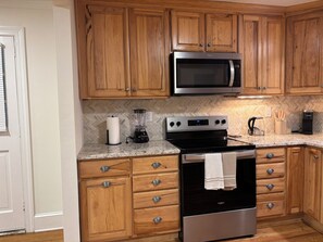 A kitchen with wooden cabinets, a microwave, a stove, and a coffee maker. - Private bathroom + bedroom UNC & Duke Hospital (Durham)