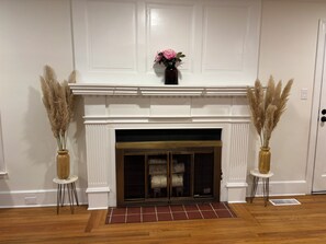 A fireplace with a white mantel, flanked by two tall vases with dried plants, and a small rug in front. - Private bathroom + bedroom UNC & Duke Hospital (Durham)