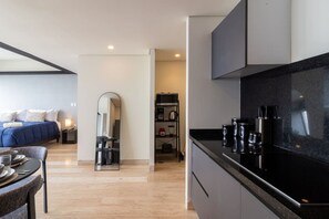 Ein modernes Hotelzimmer mit Bett, Essecke, Küche und Spiegel.