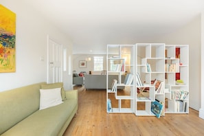 Ein Wohnzimmer mit einem grünen Sofa, einem weißen Bücherregal und einem Holzboden.