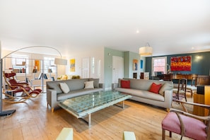 A modern living room with a glass coffee table, two sofas, a reading chair, and a desk with a chair. - GuestReady - Elegant Retreat Near Greenwich Park (London)