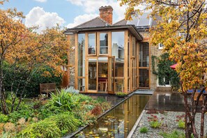 A modern house with large glass windows, a garden with a pond, and a brick chimney. - GuestReady - Elegant Retreat Near Greenwich Park (London)