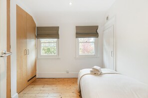 A bedroom with a bed, two windows, a wardrobe, and a radiator. - GuestReady - Elegant Retreat Near Greenwich Park (London)