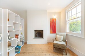 A room with a fireplace, a bookshelf, a chair, and a window with a view. - GuestReady - Elegant Retreat Near Greenwich Park (London)