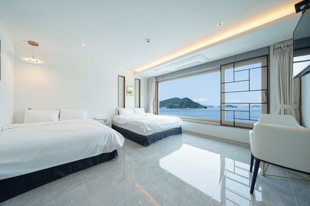Une chambre d’hôtel moderne avec deux lits, une grande fenêtre donnant sur la mer et un coin salon.