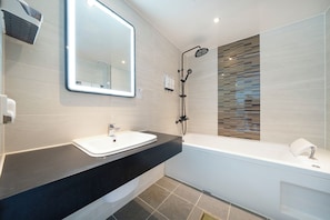 Une salle de bain moderne avec un plan de toilette noir, un lavabo blanc, un grand miroir et un espace douche.