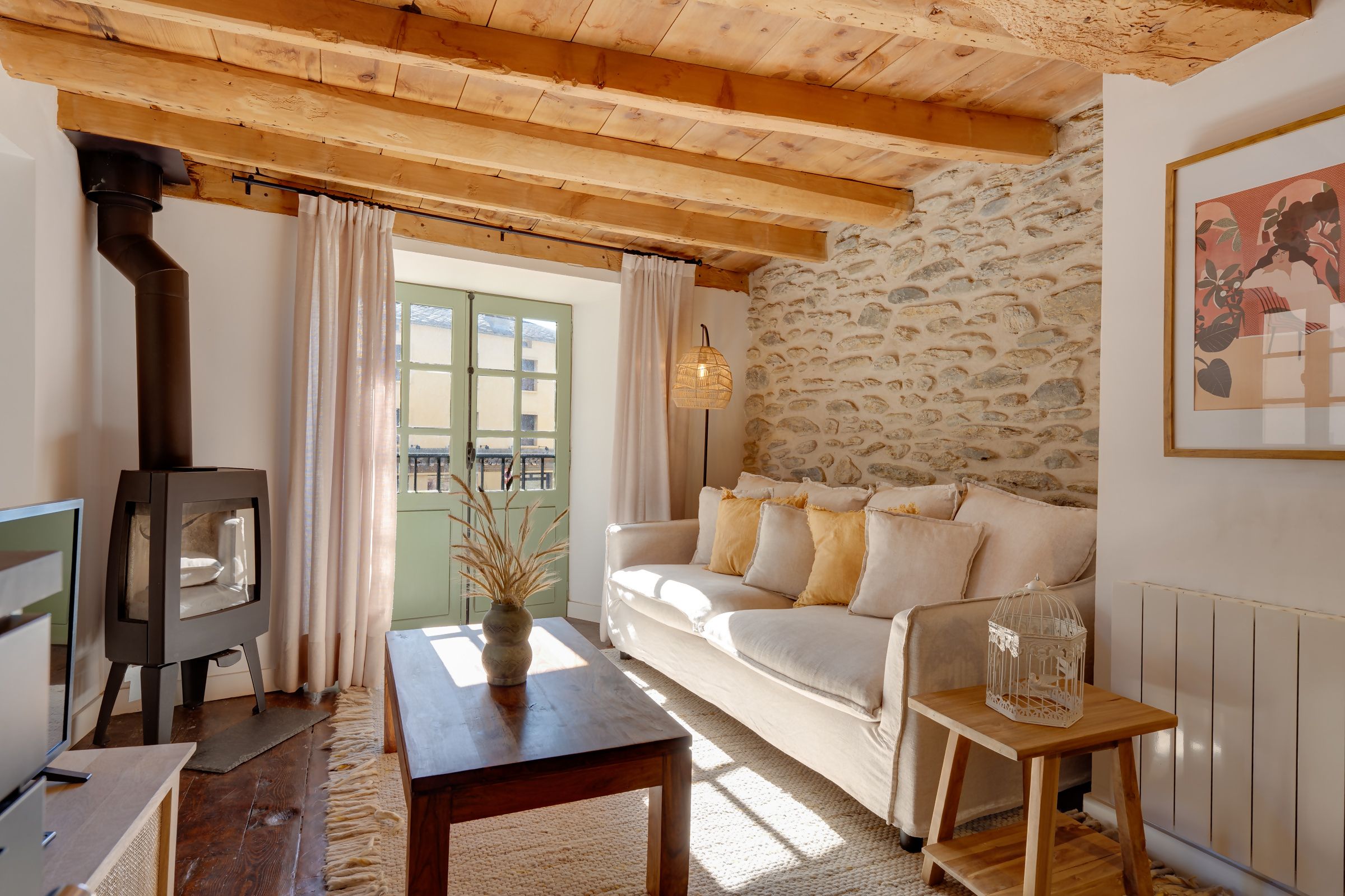 A cozy living room with a stone wall, a wooden ceiling, a sofa, a table, and a fireplace.