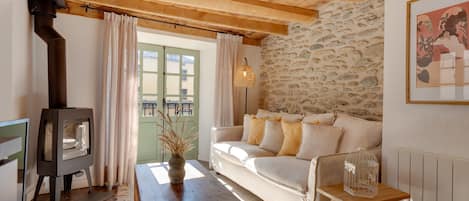 A cozy living room with a stone wall, a wooden ceiling, a sofa, a table, and a fireplace.