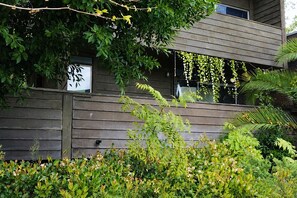 A modern building with a wooden facade, a visible window with a sign, and lush greenery in the foreground. - High-quality Condo Type: Studio City & quintessential Los Angeles lifestyle. (Studio City)