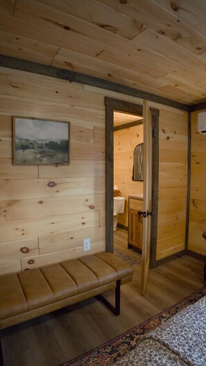 Een houten interieur met een bank, een schilderij en een zichtbare badkamer door een open deur.