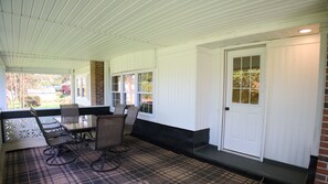 Eine überdachte Terrasse mit Tisch und Stühlen, einer Tür und Fenstern.