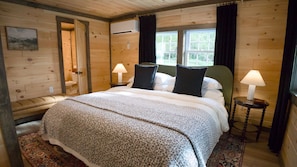 Ein Schlafzimmer einer Holzhütte mit einem Bett, zwei Nachttischlampen, einem Fenster und einer Tür zu einem Badezimmer.