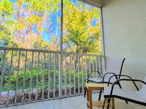 Un balcón con vistas a árboles y una mesa con dos vasos.