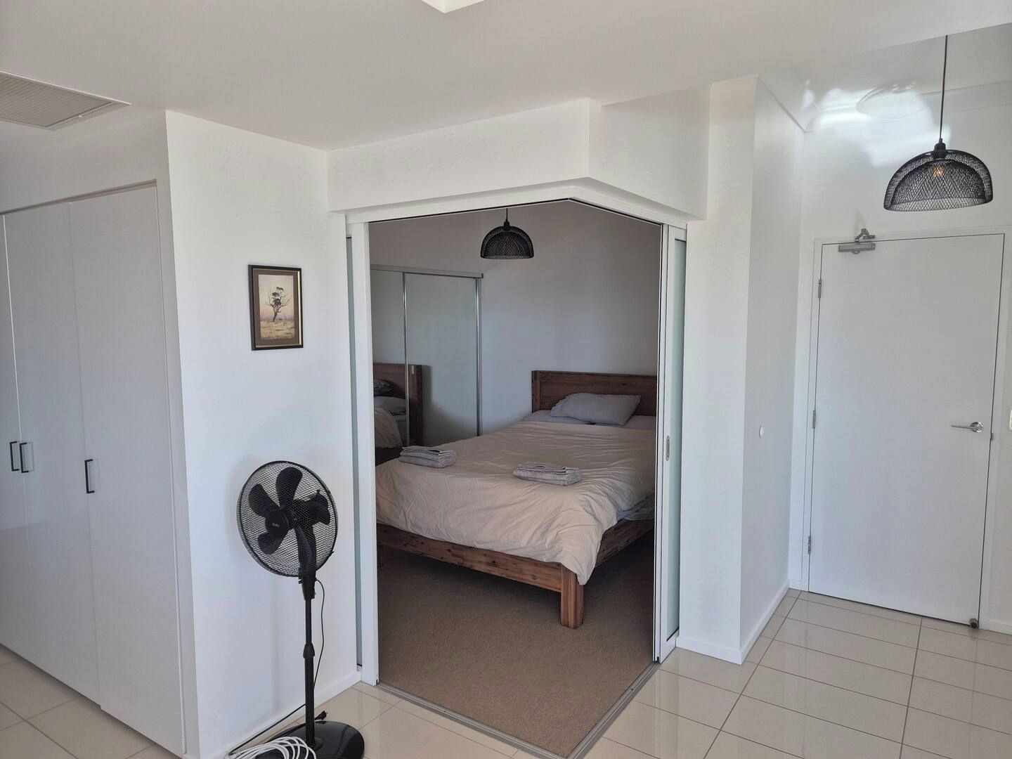 Un dormitorio con cama, ventilador, puerta y espejo.
