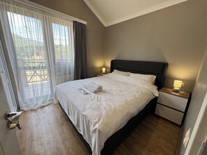 A hotel room with a bed, two bedside tables, a window with curtains, and a view of greenery outside. - 7-bedroom Villa Kazbegi-perfect for groups and families (Kazbegi)