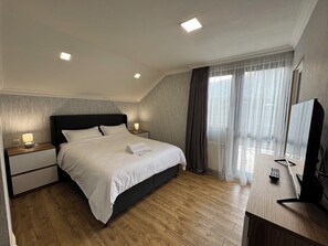 A hotel room with a bed, bedside tables, a TV, and a large window with curtains. - 7-bedroom Villa Kazbegi-perfect for groups and families (Kazbegi)