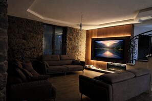 A modern living room with a stone wall, a large flat-screen TV, and a fireplace. - 7-bedroom Villa Kazbegi-perfect for groups and families (Kazbegi)
