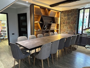 A modern dining area with a long table and chairs, a built-in wooden shelving unit, and a stone wall. - 7-bedroom Villa Kazbegi-perfect for groups and families (Kazbegi)