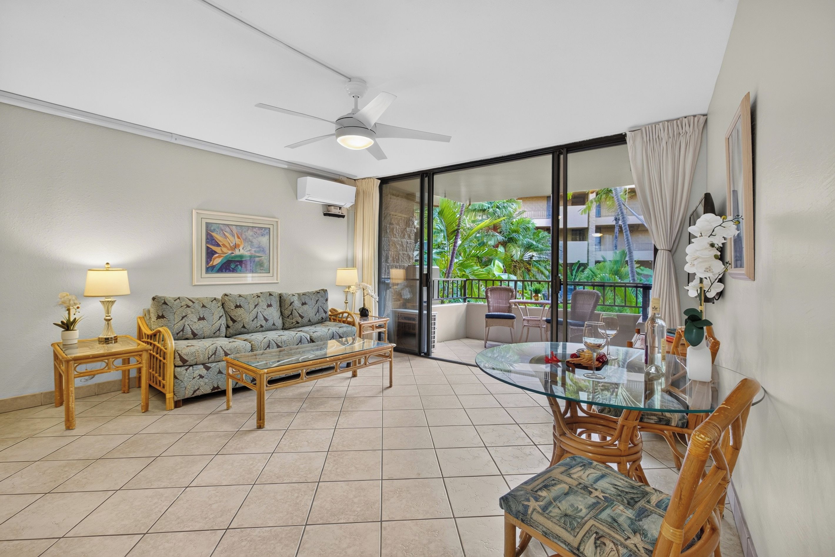 A living room with a sofa, coffee table, and chairs, a balcony with a glass door, and a ceiling fan.