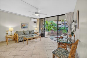 A living room with a sofa, coffee table, and chairs, a balcony with a glass door, and a ceiling fan. - Tropical Beach Oasis | Private Pool, Hot Tub & AC (Lahaina)