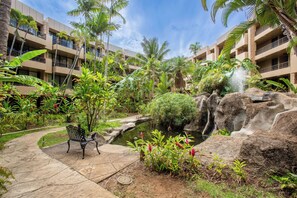 A hotel courtyard with a water feature, a bench, and lush tropical vegetation. - Tropical Beach Oasis | Private Pool, Hot Tub & AC (Lahaina)