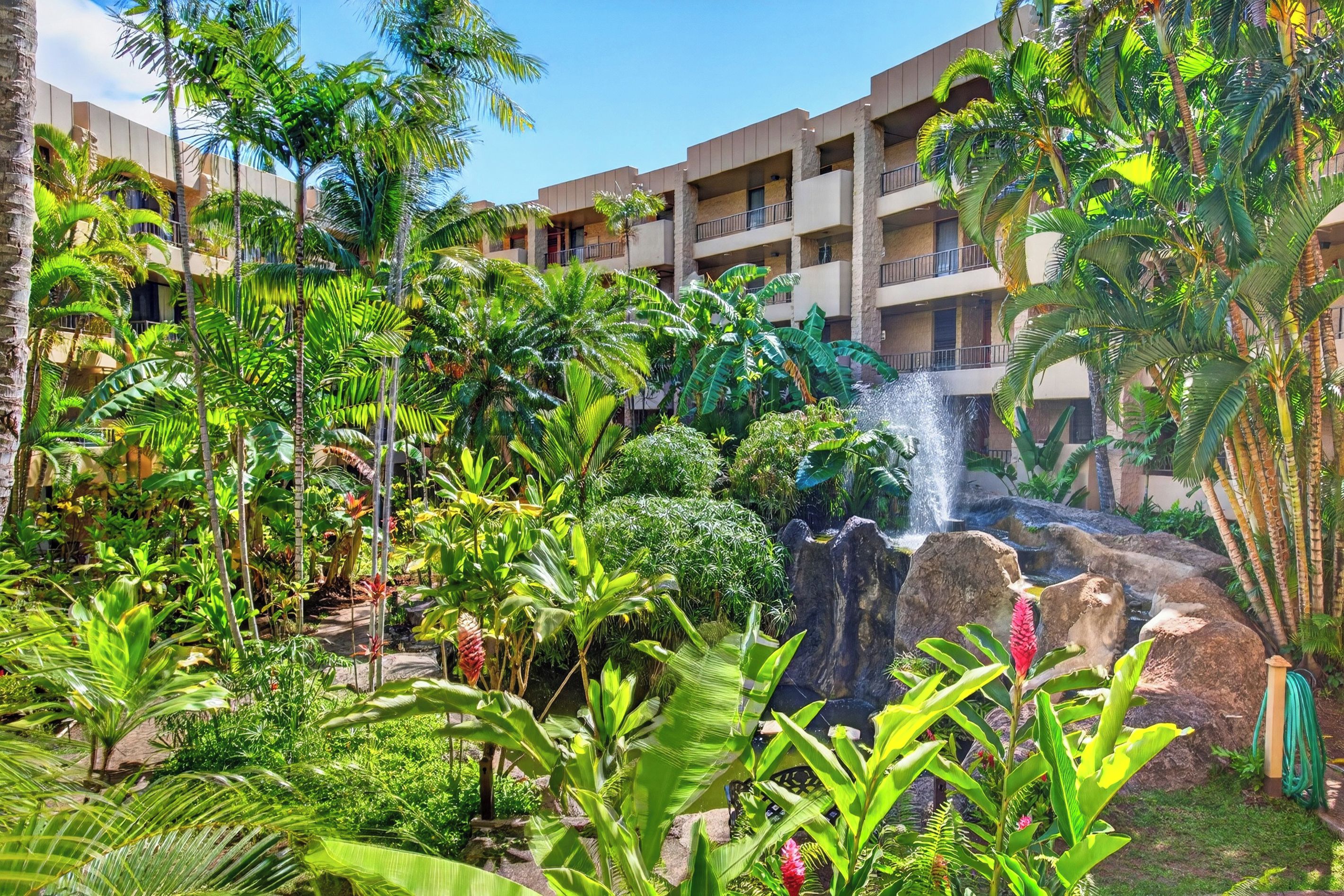 A hotel with multiple balconies, lush tropical vegetation, and a waterfall feature.