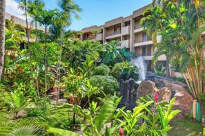 A hotel with multiple balconies, lush tropical vegetation, and a waterfall feature. - Tropical Beach Oasis | Private Pool, Hot Tub & AC (Lahaina)