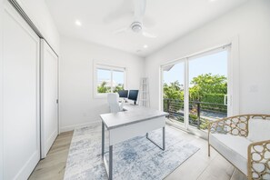 A modern room with a desk, computer, and a view of greenery through large windows. - Luxury Home +Carriage house | Waterfront| Pool 5bd (Marathon)