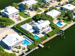 A residential area with multiple houses, a swimming pool, and a dock extending into a body of water. - Luxury Home +Carriage house | Waterfront| Pool 5bd (Marathon)