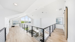 A spacious interior with a high ceiling, a staircase with a black railing, and large windows offering views of greenery. - Luxury Home +Carriage house | Waterfront| Pool 5bd (Marathon)